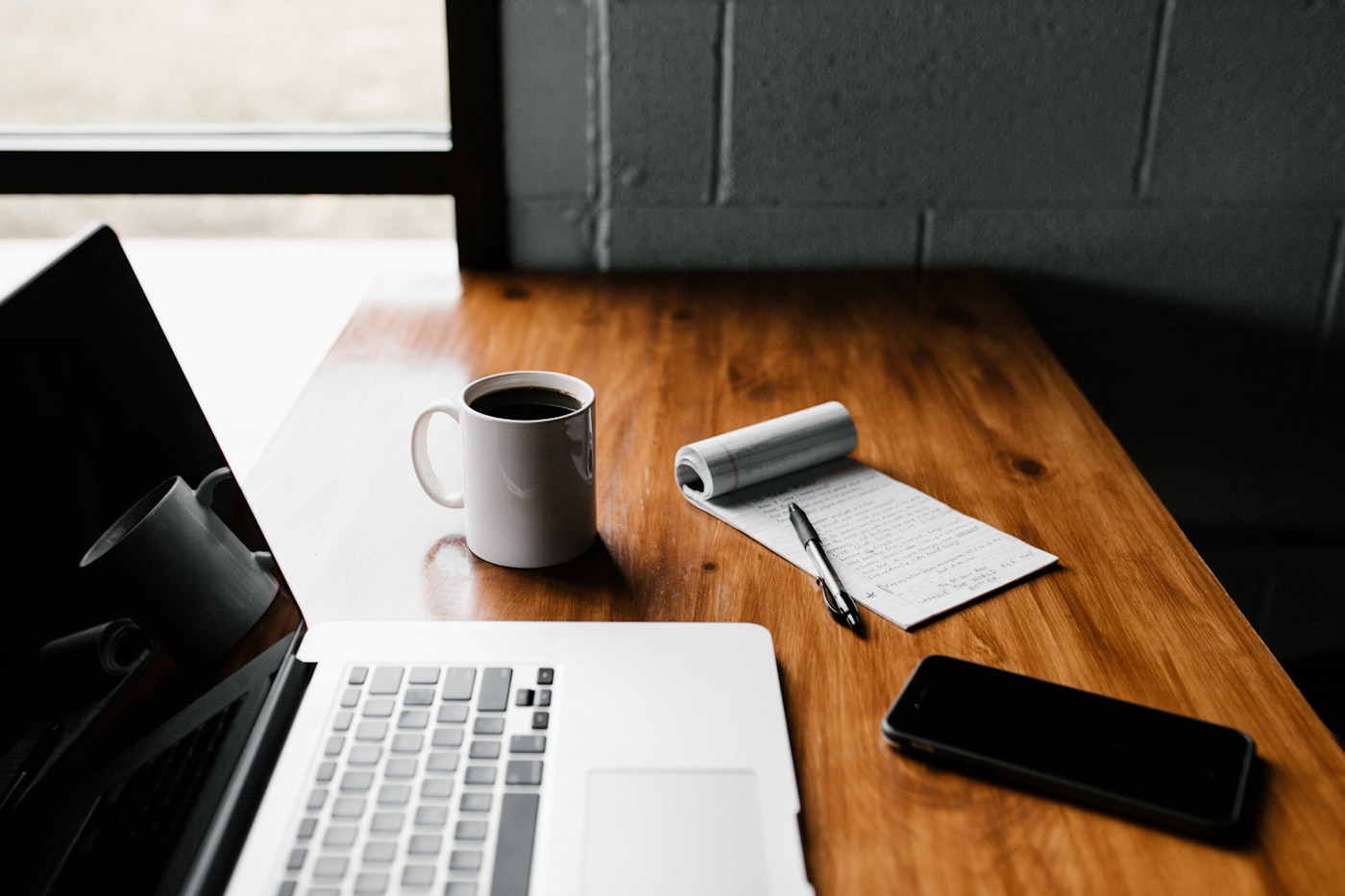 A laptop, coffee, and a handwritten notebook on a warm wood desk
